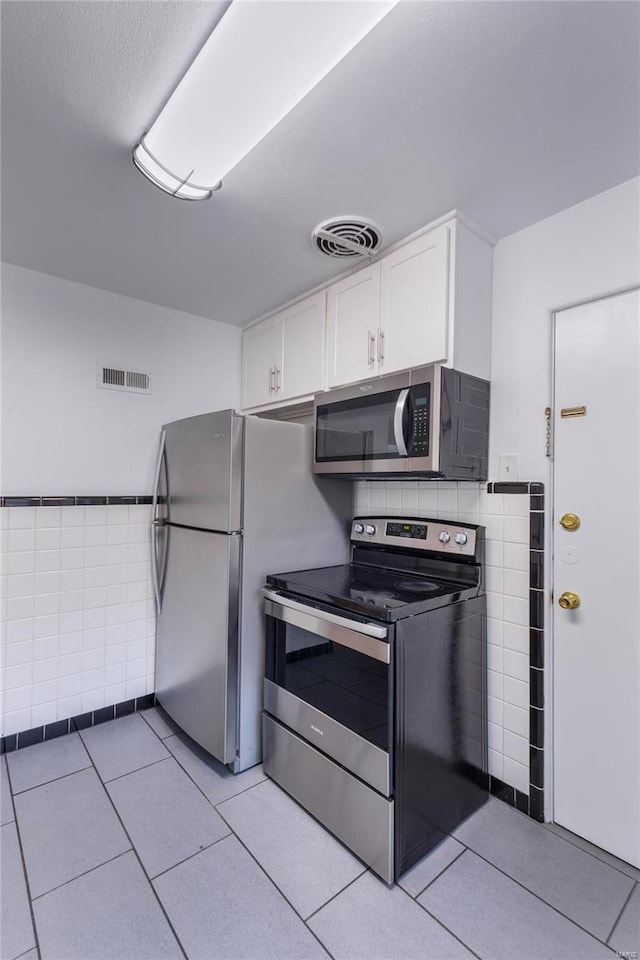 kitchen featuring tile walls, white cabinetry, appliances with stainless steel finishes, and light tile patterned floors