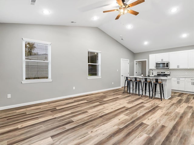 unfurnished living room featuring light wood-type flooring, vaulted ceiling, ceiling fan, and sink