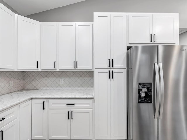 kitchen with white cabinets, stainless steel refrigerator with ice dispenser, and vaulted ceiling