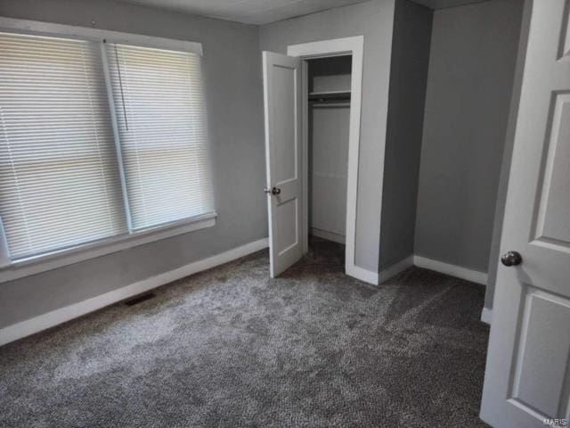 unfurnished bedroom with a closet, multiple windows, and dark carpet