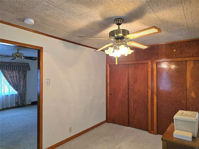 unfurnished bedroom with carpet flooring, ceiling fan, wooden walls, and ornamental molding