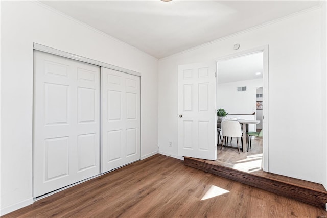 unfurnished bedroom with crown molding, a closet, and wood-type flooring