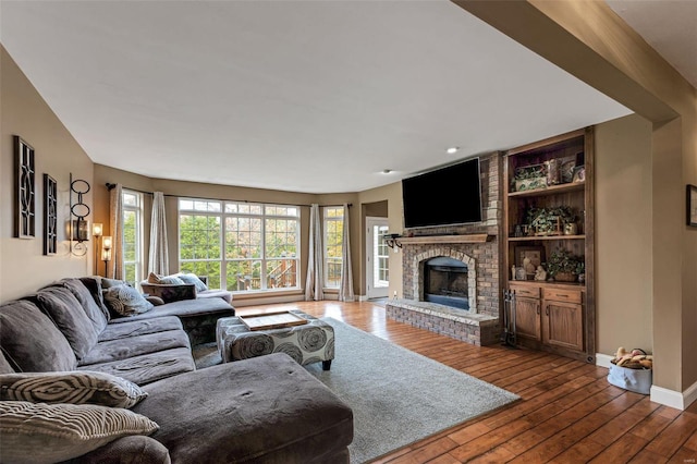 living room with built in features, wood-type flooring, and a brick fireplace