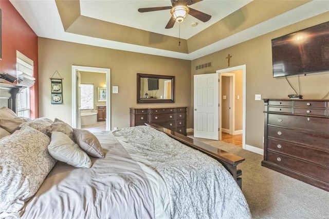 bedroom featuring a raised ceiling, ensuite bath, ceiling fan, and light carpet