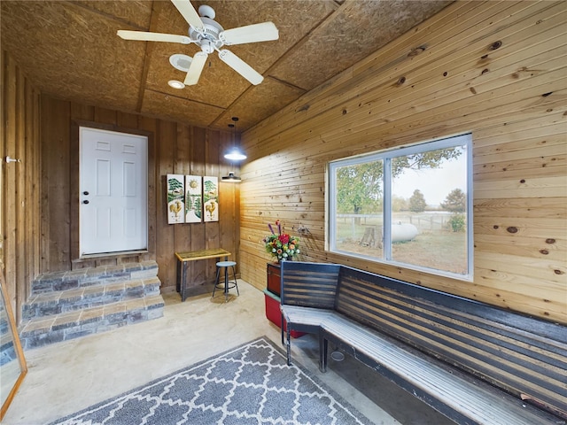 living area with ceiling fan, wooden walls, and concrete floors