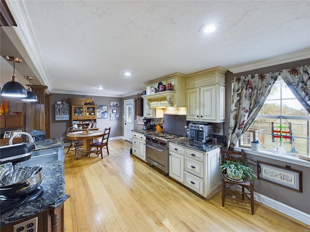 kitchen featuring hanging light fixtures, ornamental molding, dark stone counters, stainless steel stove, and light wood-type flooring