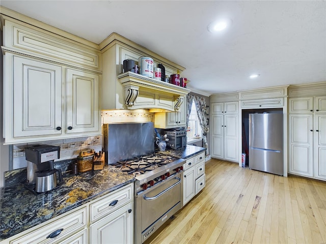 kitchen featuring appliances with stainless steel finishes, light wood-type flooring, backsplash, dark stone counters, and cream cabinetry