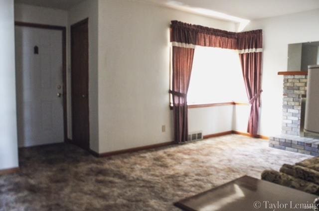 unfurnished living room featuring a brick fireplace and dark colored carpet