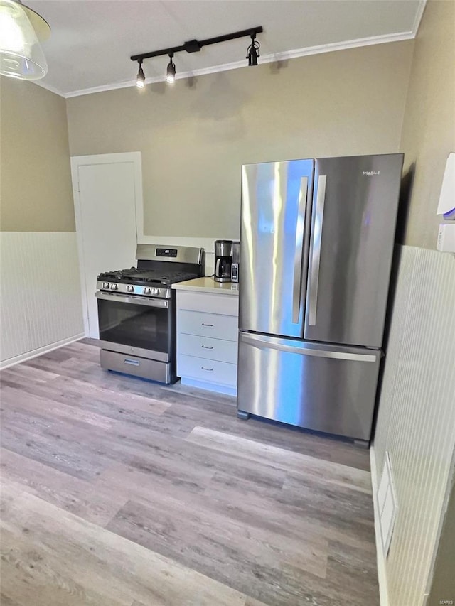 kitchen with white cabinets, crown molding, stainless steel appliances, and light hardwood / wood-style flooring