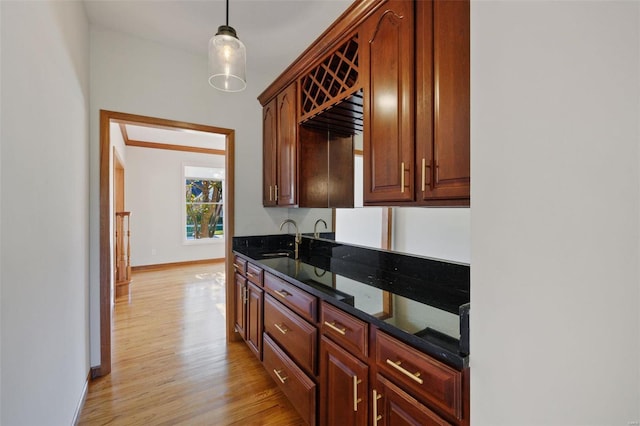 kitchen featuring dark stone countertops, sink, pendant lighting, and light wood-type flooring