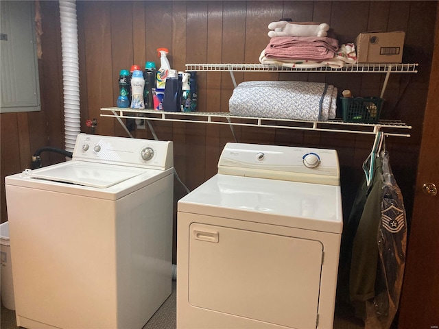 clothes washing area featuring wood walls, electric panel, and washing machine and clothes dryer