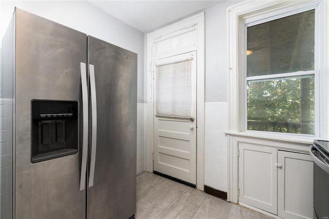 kitchen featuring white cabinetry, stainless steel refrigerator with ice dispenser, and tile walls