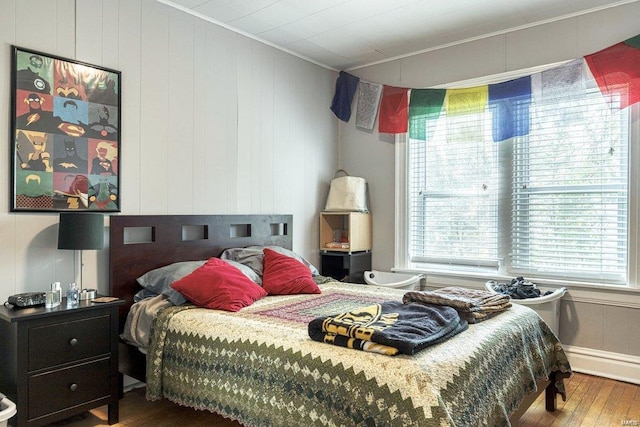 bedroom with hardwood / wood-style floors, ornamental molding, and wood walls