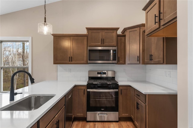 kitchen featuring lofted ceiling, sink, tasteful backsplash, decorative light fixtures, and stainless steel appliances