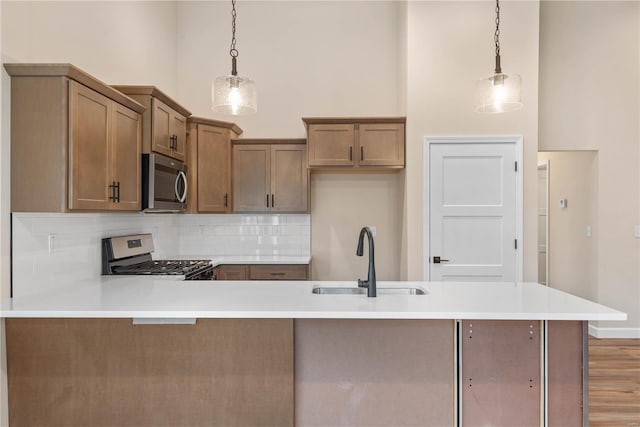 kitchen featuring sink, stainless steel appliances, a towering ceiling, decorative light fixtures, and decorative backsplash