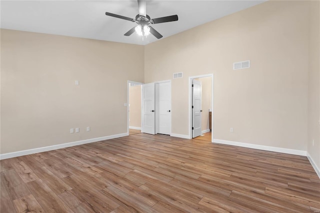 unfurnished bedroom with ceiling fan, a high ceiling, and light hardwood / wood-style flooring