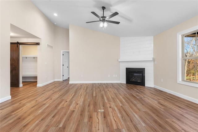 unfurnished living room featuring ceiling fan, a large fireplace, a barn door, light hardwood / wood-style floors, and vaulted ceiling