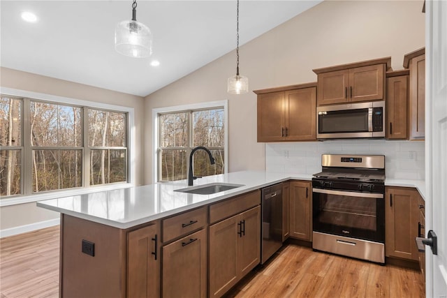 kitchen featuring kitchen peninsula, pendant lighting, stainless steel appliances, and sink