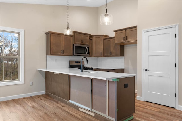 kitchen with stainless steel appliances, light hardwood / wood-style flooring, backsplash, kitchen peninsula, and pendant lighting