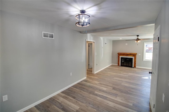 unfurnished living room with ceiling fan with notable chandelier and light hardwood / wood-style flooring