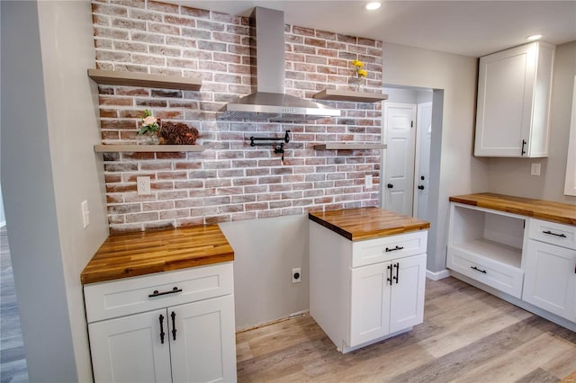 kitchen featuring white cabinets, light hardwood / wood-style floors, wall chimney range hood, and wood counters