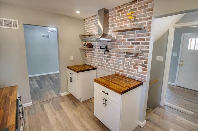 kitchen with butcher block countertops, wall chimney exhaust hood, light hardwood / wood-style floors, and white cabinets