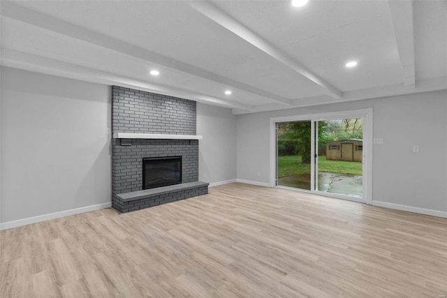 unfurnished living room featuring beamed ceiling, light wood-type flooring, and a brick fireplace