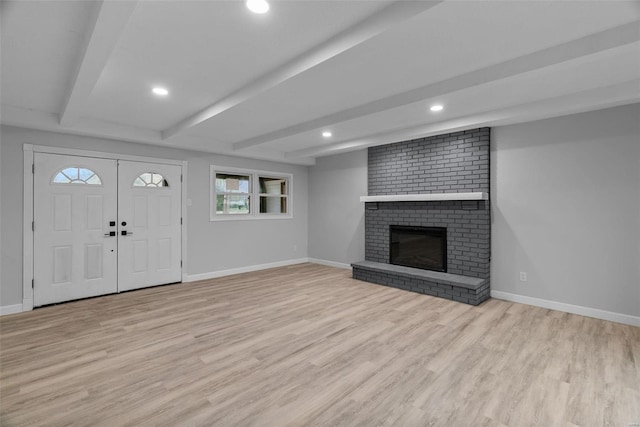 unfurnished living room with beamed ceiling, light hardwood / wood-style floors, and a brick fireplace