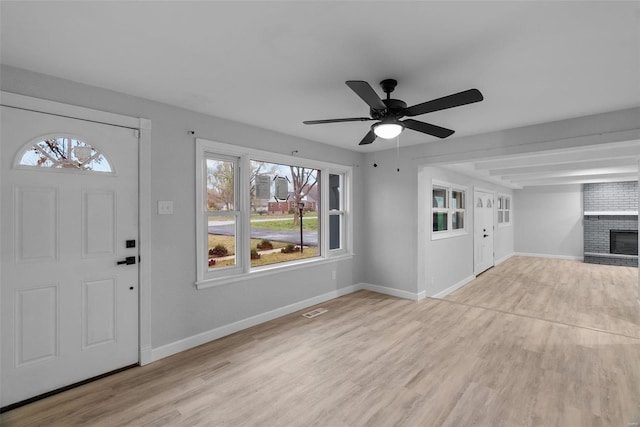 foyer entrance with ceiling fan, light wood-type flooring, and a fireplace