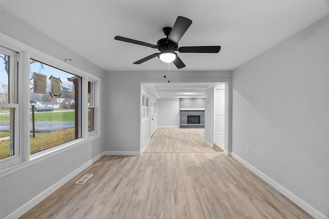 unfurnished living room featuring ceiling fan, light wood-type flooring, and a brick fireplace