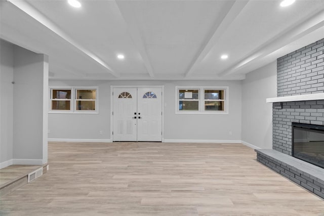 entryway featuring light hardwood / wood-style floors, beam ceiling, and a brick fireplace