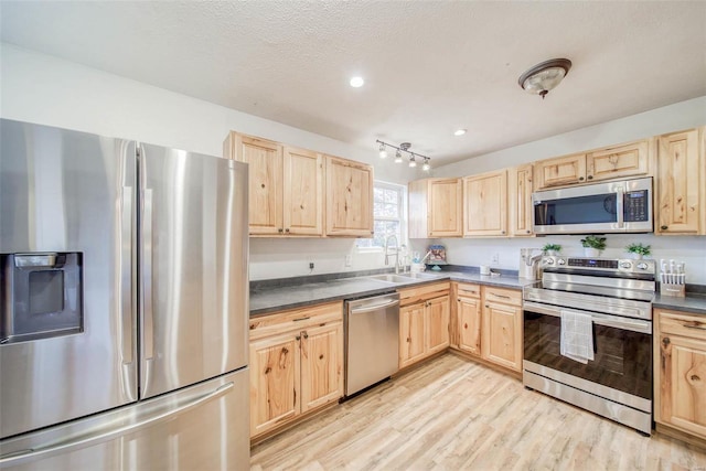 kitchen with sink, appliances with stainless steel finishes, light brown cabinets, a textured ceiling, and light wood-type flooring