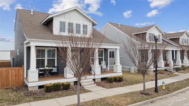 view of front of house featuring a porch, a shingled roof, and fence