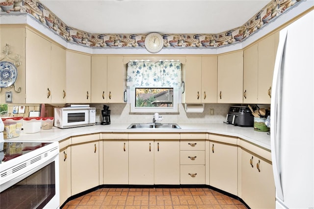 kitchen with tasteful backsplash, cream cabinets, sink, and white appliances