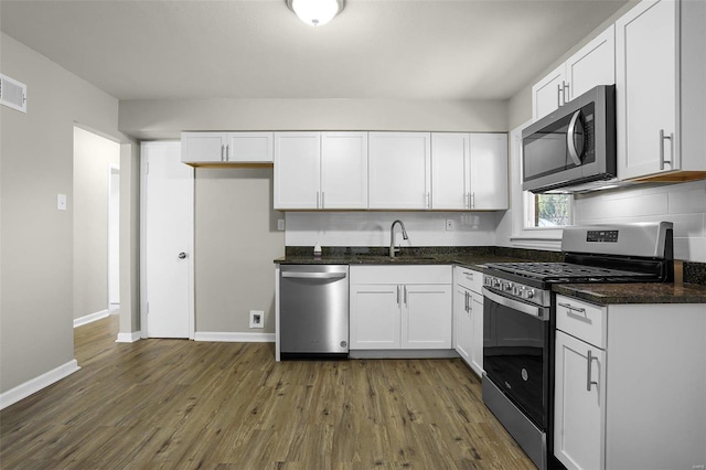 kitchen with stainless steel appliances, dark hardwood / wood-style flooring, sink, white cabinetry, and dark stone countertops