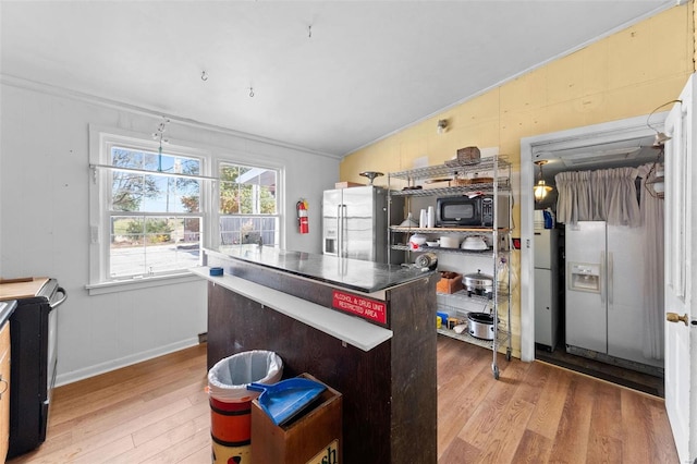 kitchen featuring ornamental molding, stainless steel fridge, a kitchen island, light wood-type flooring, and vaulted ceiling