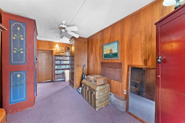 interior space with ceiling fan, wooden walls, and carpet