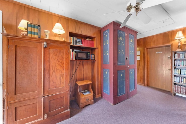 interior space with built in features, wood walls, and ceiling fan