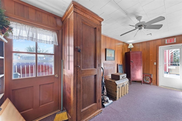 doorway to outside featuring wood walls, ceiling fan, and carpet floors