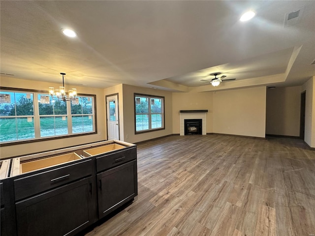 kitchen with hardwood / wood-style flooring, ceiling fan with notable chandelier, pendant lighting, and a tray ceiling