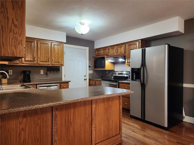 kitchen with sink, stainless steel appliances, light hardwood / wood-style flooring, kitchen peninsula, and a textured ceiling