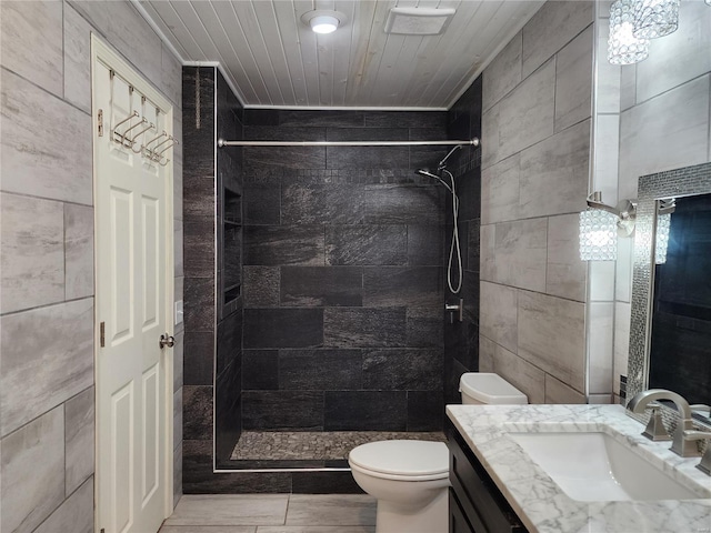 bathroom with vanity, toilet, tiled shower, and tile walls