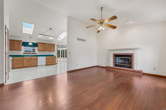 unfurnished living room featuring sink, a brick fireplace, high vaulted ceiling, ceiling fan, and light wood-type flooring