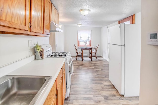 kitchen with white appliances, a textured ceiling, sink, and light hardwood / wood-style floors