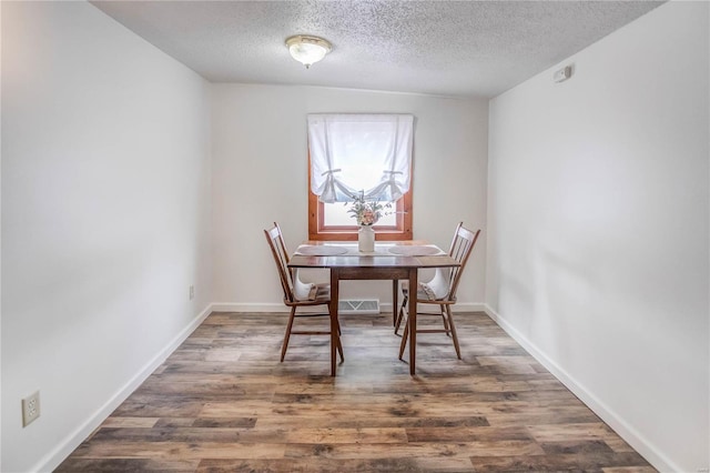 dining space with dark wood-type flooring, a textured ceiling, and vaulted ceiling