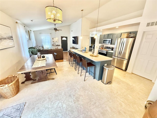 kitchen with gray cabinetry, stainless steel appliances, a kitchen island, pendant lighting, and vaulted ceiling