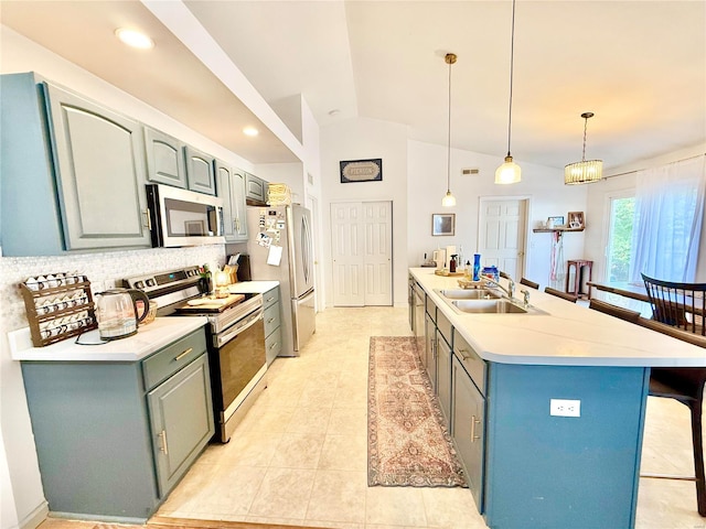 kitchen with stainless steel appliances, sink, decorative light fixtures, an island with sink, and vaulted ceiling