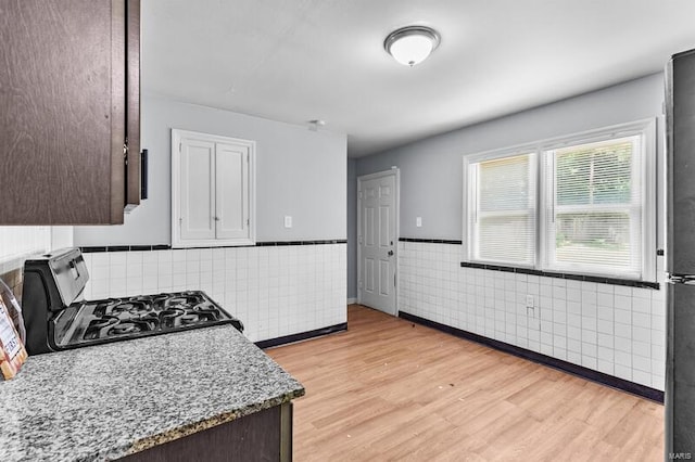 kitchen with dark brown cabinetry, light hardwood / wood-style floors, light stone countertops, stove, and tile walls