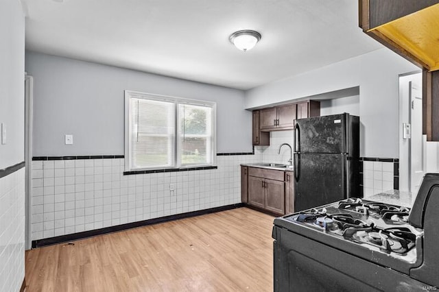 kitchen with black appliances, tile walls, dark brown cabinetry, sink, and light hardwood / wood-style flooring