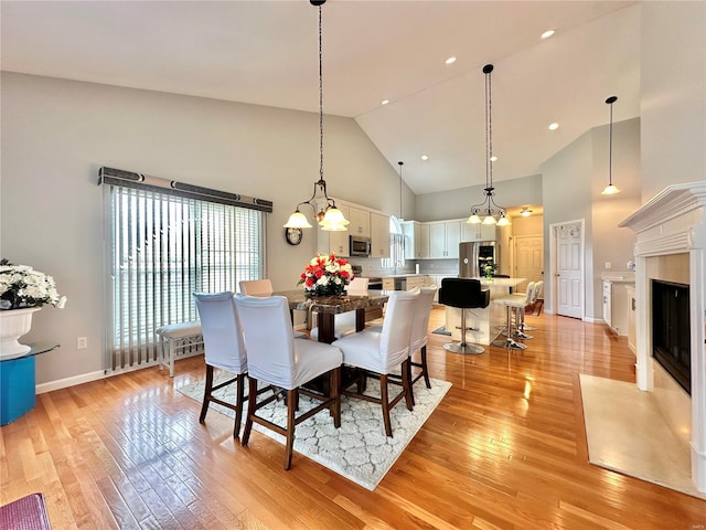 dining room with light hardwood / wood-style floors, high vaulted ceiling, and a notable chandelier